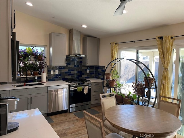 kitchen with appliances with stainless steel finishes, wall chimney exhaust hood, and gray cabinetry