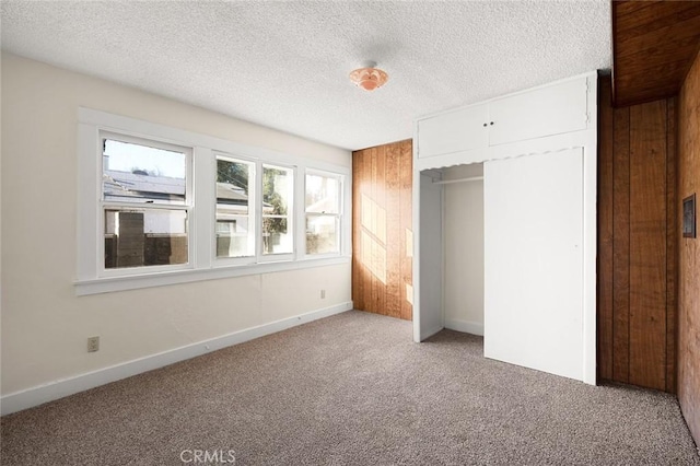 unfurnished bedroom featuring carpet, a closet, wood walls, and a textured ceiling