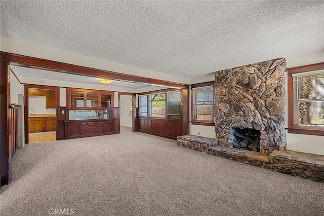 unfurnished living room featuring carpet floors, a stone fireplace, and a textured ceiling