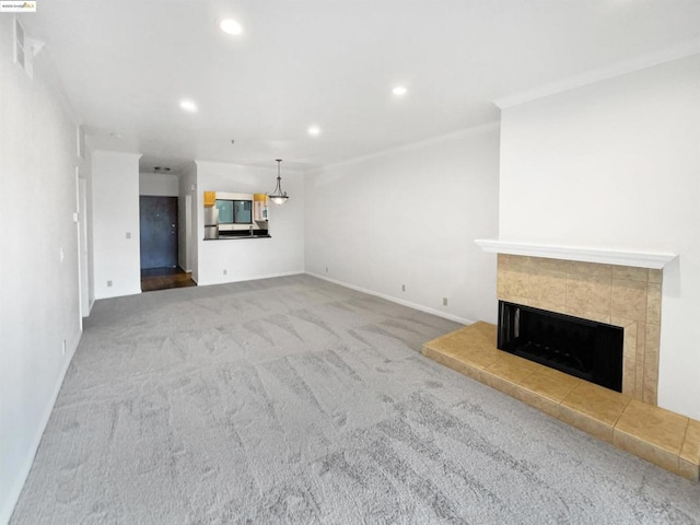 unfurnished living room with a tiled fireplace, ornamental molding, and carpet