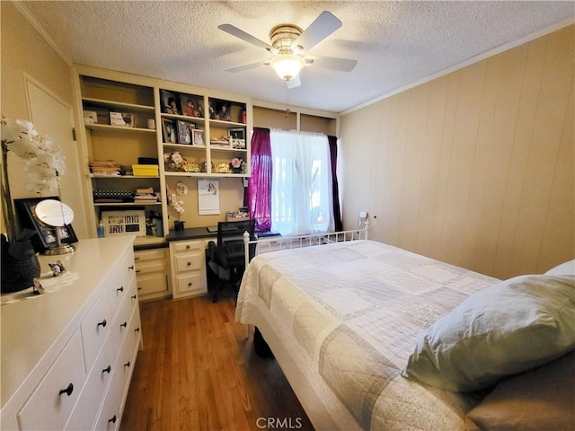 bedroom featuring ceiling fan, dark wood-type flooring, ornamental molding, wooden walls, and a textured ceiling