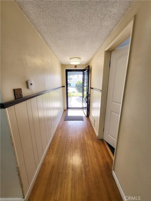 hall with a textured ceiling and light wood-type flooring