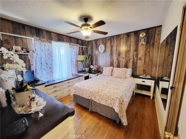 bedroom featuring ceiling fan, light hardwood / wood-style floors, wooden walls, and a textured ceiling