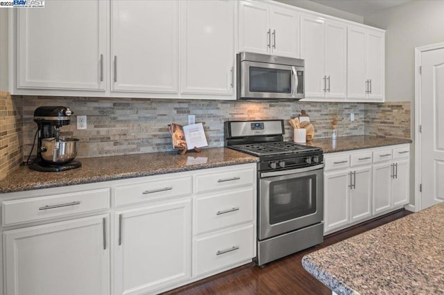 kitchen with white cabinetry, dark stone countertops, backsplash, dark hardwood / wood-style flooring, and stainless steel appliances