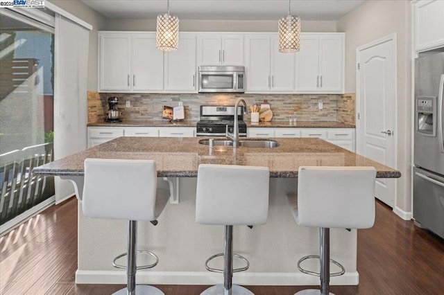 kitchen featuring appliances with stainless steel finishes, a kitchen island with sink, hanging light fixtures, and white cabinets