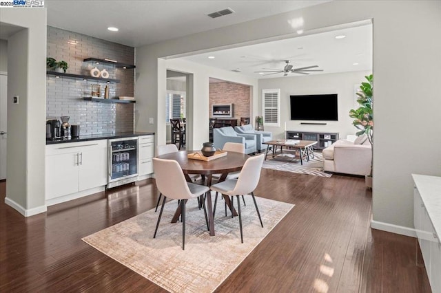 dining area with bar, beverage cooler, dark hardwood / wood-style flooring, ceiling fan, and a fireplace