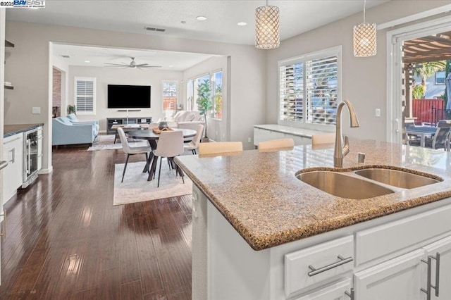 kitchen featuring sink, white cabinetry, hanging light fixtures, light stone countertops, and an island with sink