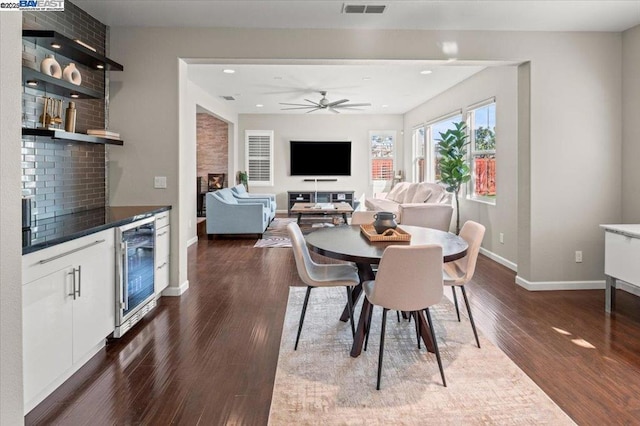 dining area featuring wine cooler, dark hardwood / wood-style flooring, a large fireplace, and ceiling fan