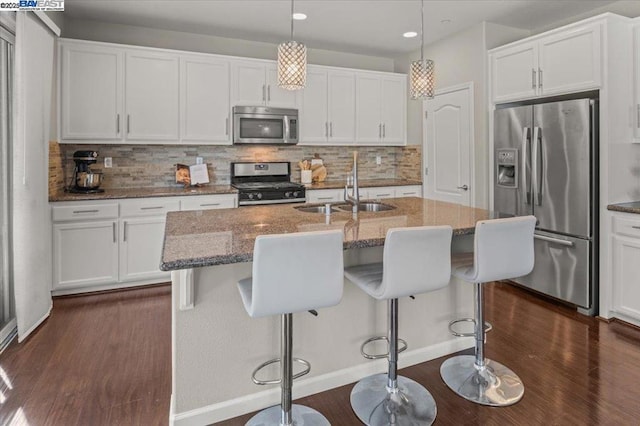 kitchen with sink, a kitchen island with sink, hanging light fixtures, stainless steel appliances, and white cabinets