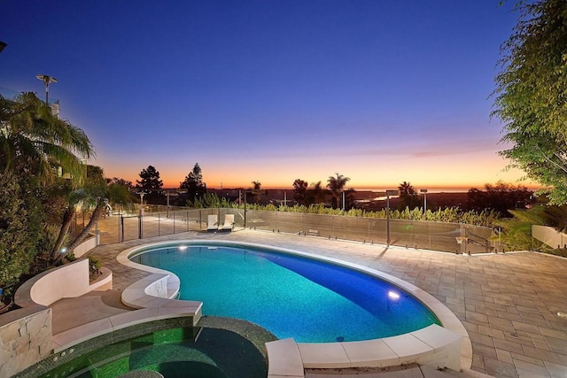 pool at dusk with an in ground hot tub and a patio area