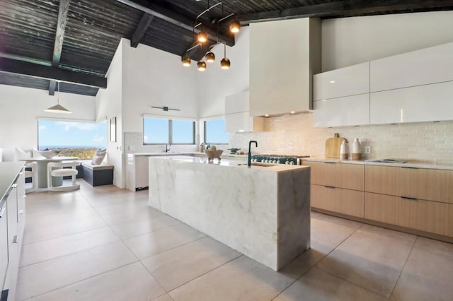 kitchen with hanging light fixtures, an island with sink, beamed ceiling, high vaulted ceiling, and light brown cabinets