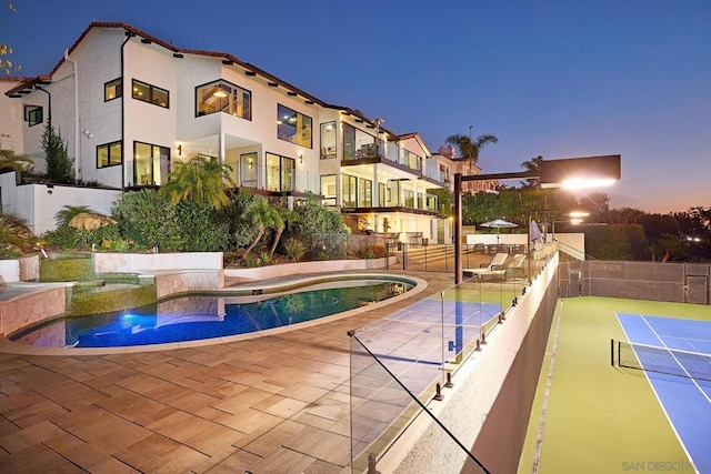 pool at dusk featuring a patio and tennis court