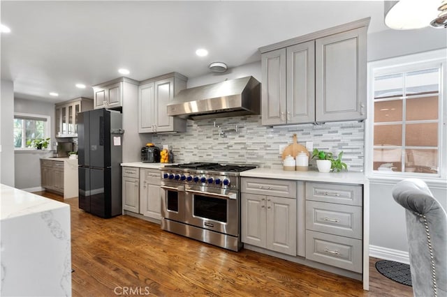 kitchen with dark wood-style floors, backsplash, freestanding refrigerator, wall chimney range hood, and double oven range