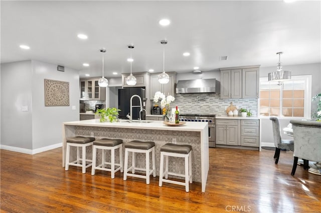 kitchen featuring high end stainless steel range, gray cabinetry, freestanding refrigerator, a kitchen island with sink, and wall chimney range hood