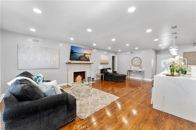 living room with recessed lighting, visible vents, a lit fireplace, and wood finished floors