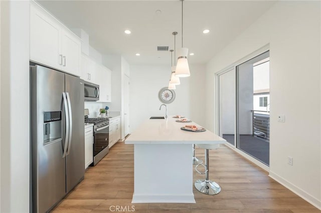 kitchen featuring appliances with stainless steel finishes, light wood-type flooring, white cabinets, pendant lighting, and a center island with sink