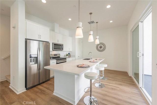 kitchen with decorative light fixtures, sink, white cabinetry, a kitchen island with sink, and stainless steel appliances