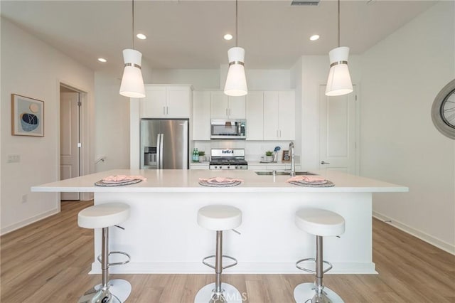 kitchen featuring white cabinets, stainless steel appliances, pendant lighting, and a large island with sink