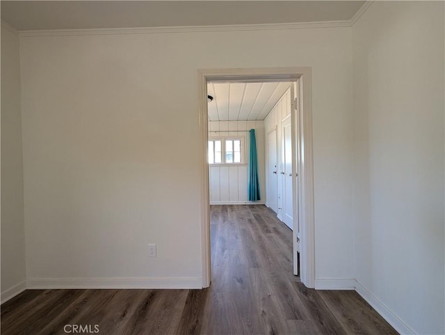 spare room featuring dark wood-style flooring, crown molding, and baseboards