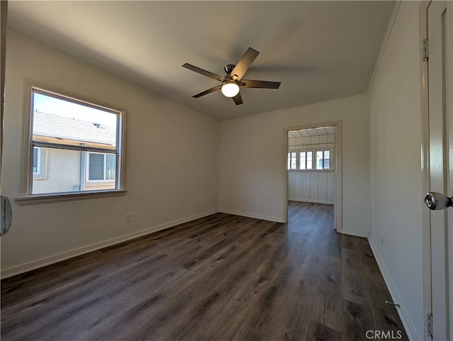 empty room featuring dark wood-type flooring, a ceiling fan, and baseboards