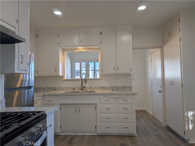 kitchen with white cabinets, light stone counters, appliances with stainless steel finishes, wood finished floors, and a sink