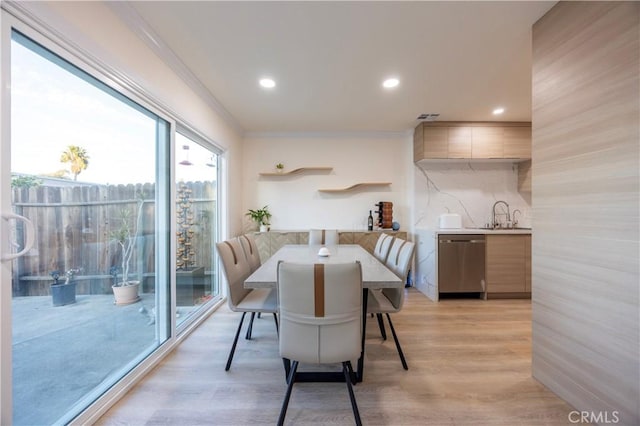 dining area featuring ornamental molding, plenty of natural light, sink, and light wood-type flooring