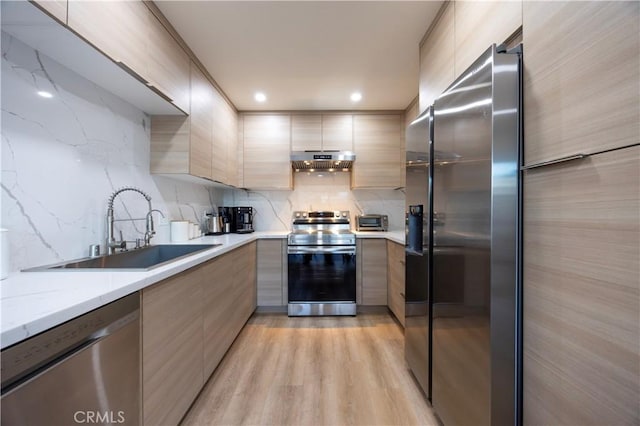 kitchen with appliances with stainless steel finishes, ventilation hood, sink, light stone counters, and light hardwood / wood-style floors