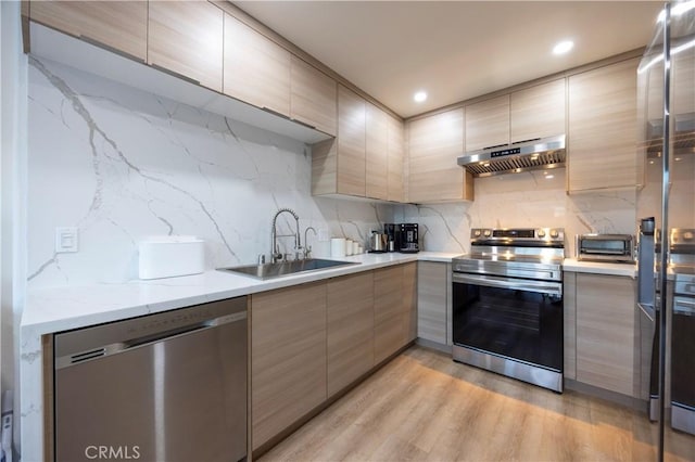 kitchen with sink, light hardwood / wood-style flooring, appliances with stainless steel finishes, tasteful backsplash, and light stone counters