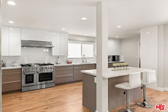 kitchen featuring white cabinetry, a kitchen breakfast bar, light wood-type flooring, range with two ovens, and range hood