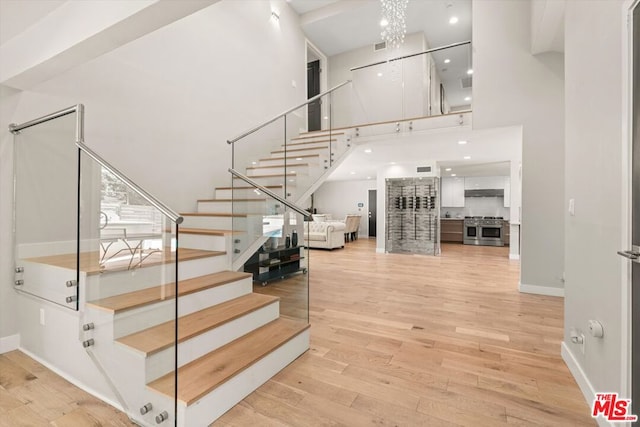 stairs with an inviting chandelier, a towering ceiling, and wood-type flooring