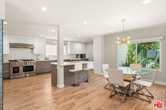 kitchen with decorative light fixtures, white cabinets, an inviting chandelier, light hardwood / wood-style floors, and range with two ovens