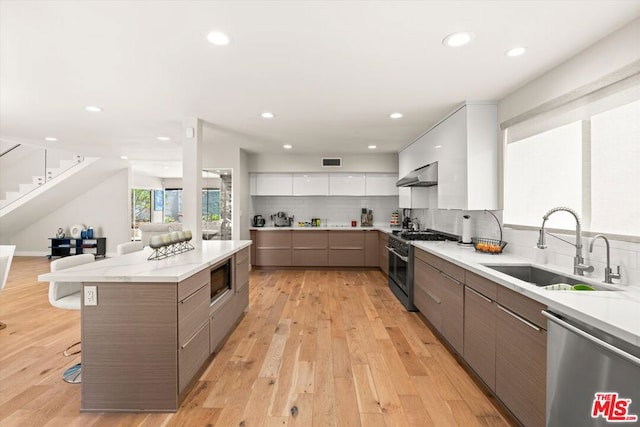 kitchen with stainless steel appliances, sink, white cabinetry, light hardwood / wood-style floors, and a breakfast bar