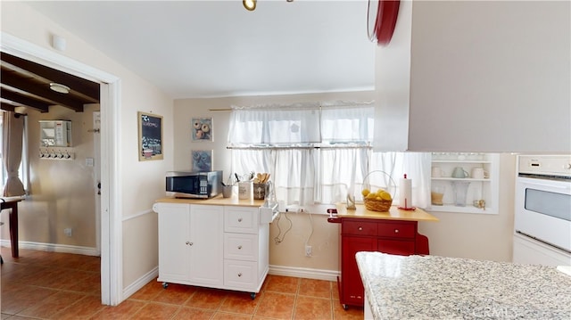 kitchen featuring double oven, light tile patterned flooring, and vaulted ceiling with beams