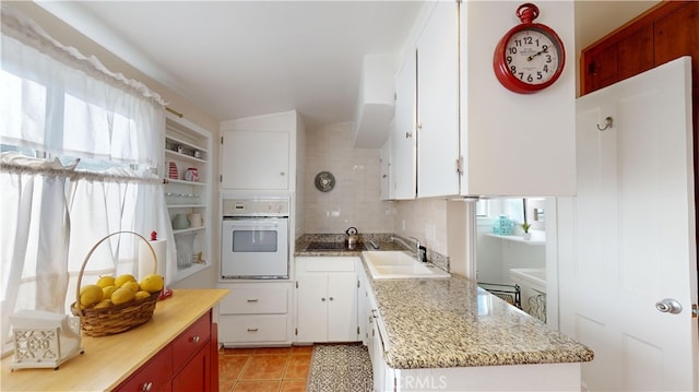 kitchen with sink, white cabinets, decorative backsplash, and oven