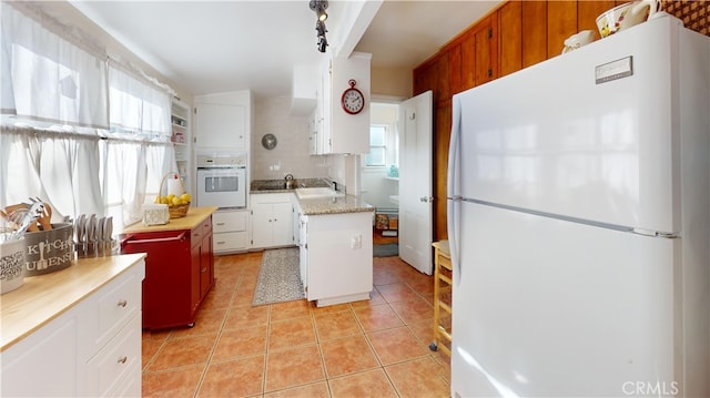 kitchen featuring white cabinets, a center island, white appliances, light tile patterned floors, and backsplash