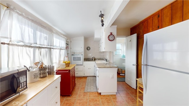 kitchen with white appliances, a center island, decorative backsplash, white cabinets, and sink