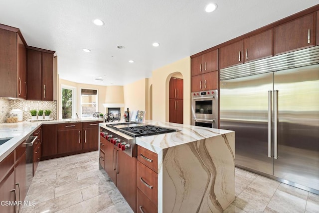 kitchen featuring light stone countertops, stainless steel appliances, decorative backsplash, and a kitchen island