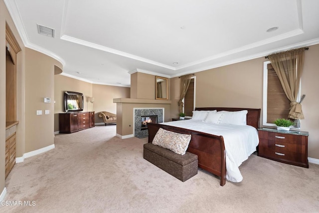 bedroom featuring a premium fireplace, light carpet, a tray ceiling, and crown molding