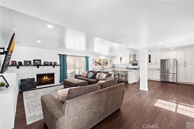 living room with dark wood-style flooring, a brick fireplace, and recessed lighting