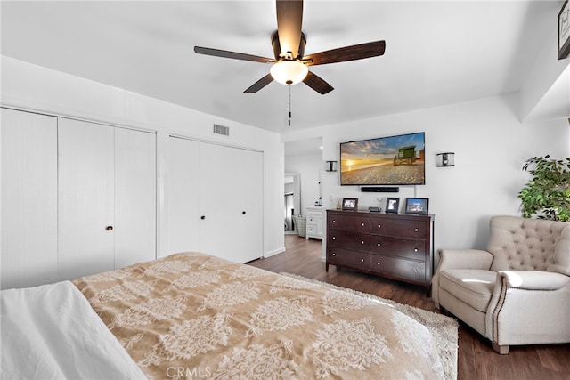 bedroom with two closets, ceiling fan, visible vents, and wood finished floors