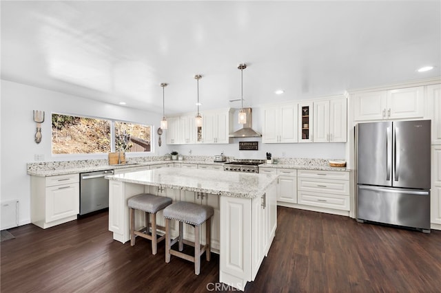 kitchen with glass insert cabinets, a center island, wall chimney exhaust hood, stainless steel appliances, and dark wood-type flooring