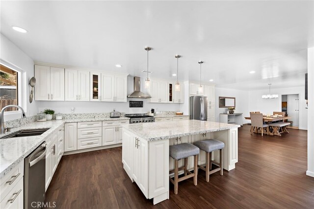 kitchen with stainless steel appliances, a kitchen island, wall chimney exhaust hood, white cabinets, and sink