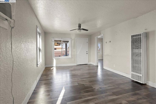 unfurnished living room with an AC wall unit, a textured ceiling, ceiling fan, and dark wood-type flooring