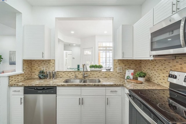 kitchen with stainless steel appliances, light stone countertops, white cabinetry, and sink