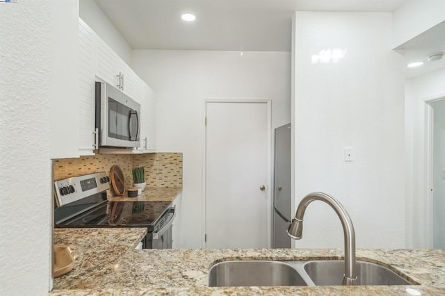 kitchen featuring stainless steel appliances, sink, white cabinets, light stone counters, and decorative backsplash