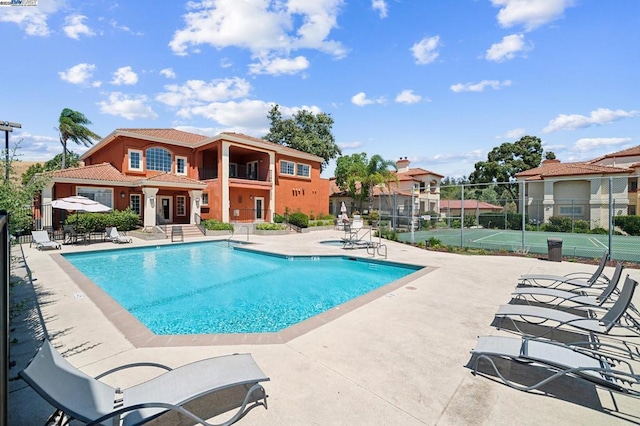 view of swimming pool featuring tennis court and a patio