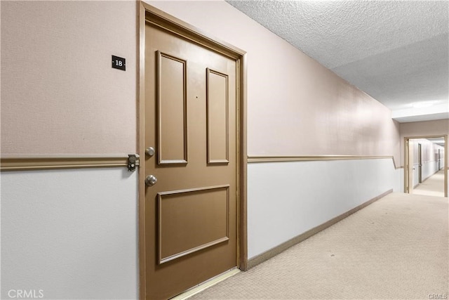 hall featuring a textured ceiling and light colored carpet