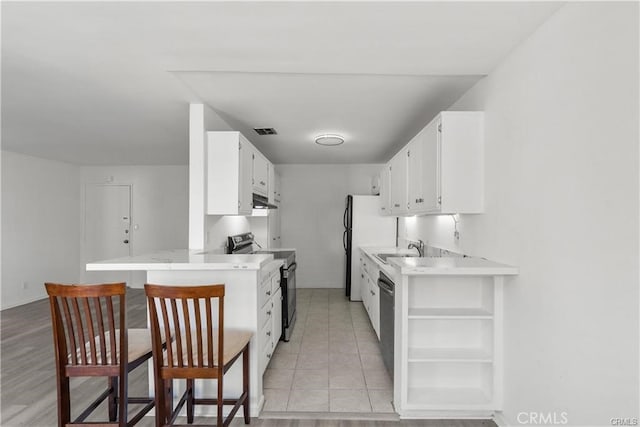 kitchen featuring kitchen peninsula, a kitchen bar, stainless steel range with electric stovetop, white cabinets, and black dishwasher