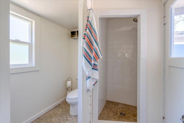 bathroom with toilet, tiled shower, and plenty of natural light