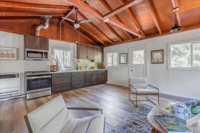 kitchen with light wood-type flooring, beam ceiling, a healthy amount of sunlight, and appliances with stainless steel finishes